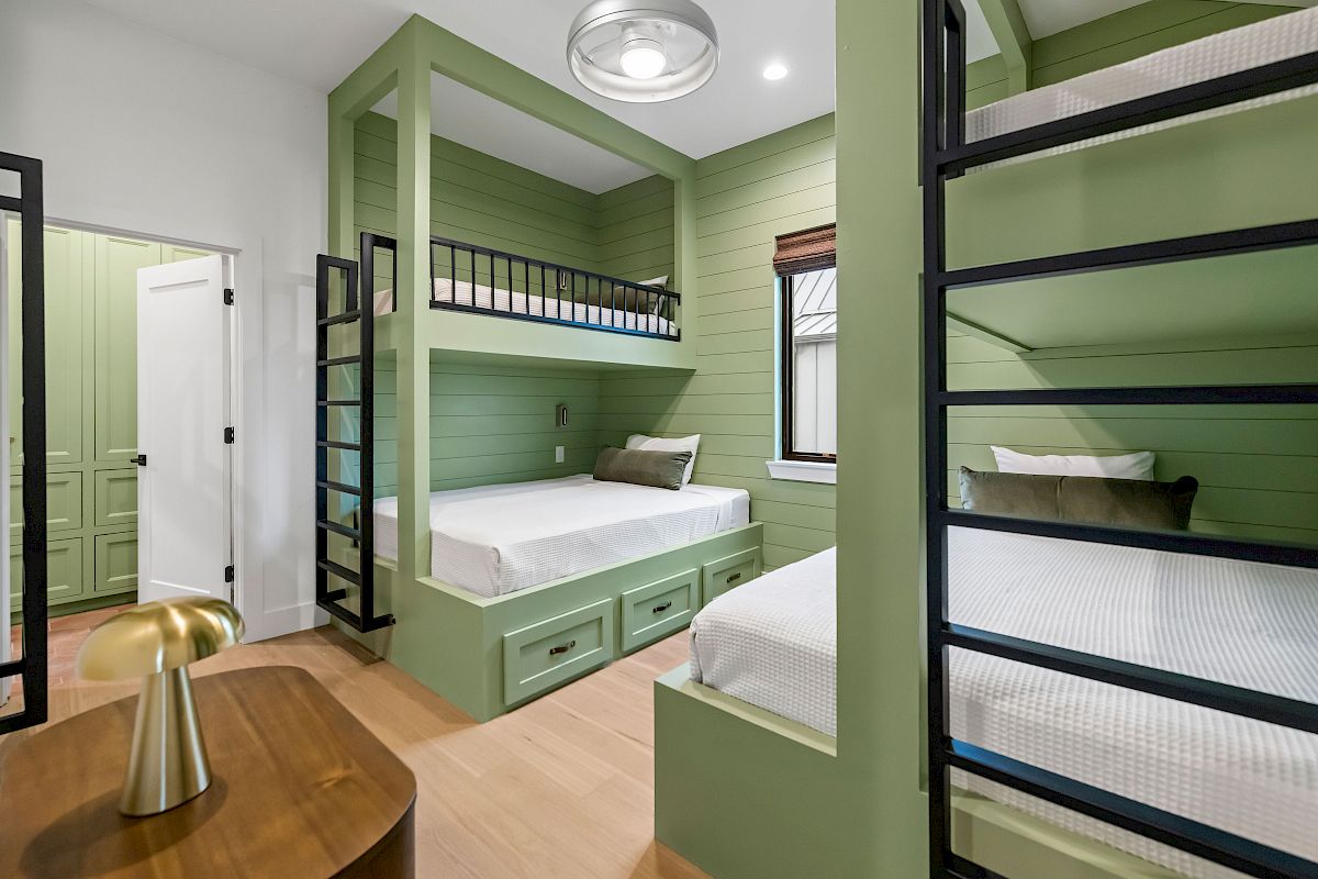 Green bunk room with built-in beds and storage under each bunk, a cozy modern cabin vibe, and a small window seat by the end of the room.