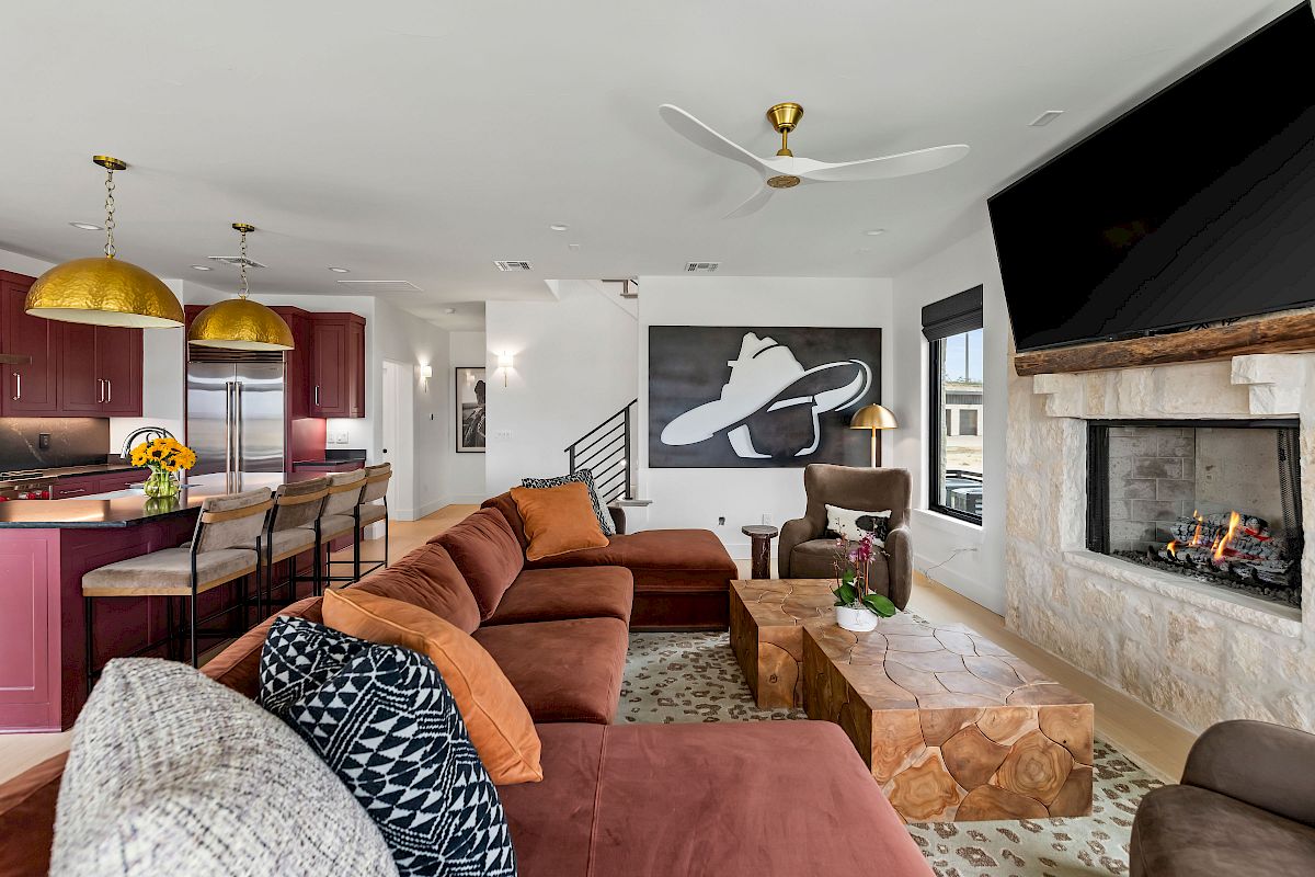 A modern, open-concept living room and kitchen with a large sectional, stone fireplace, big TV, industrial chandelier, and a bold Nike wall art, bright and cozy.