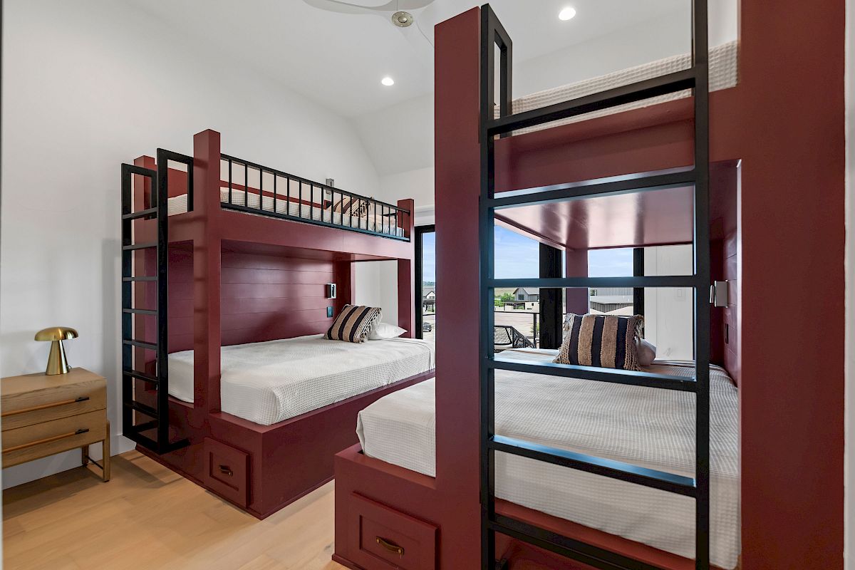 A compact dorm-style bedroom with dark wood bunk beds, matching dressers, and a small nightstand, brightened by light wood floors and white walls.