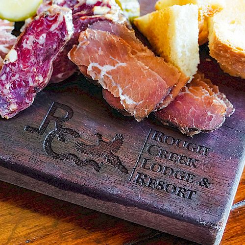 A charcuterie board with various cured meats and bread is displayed. The board is engraved with 