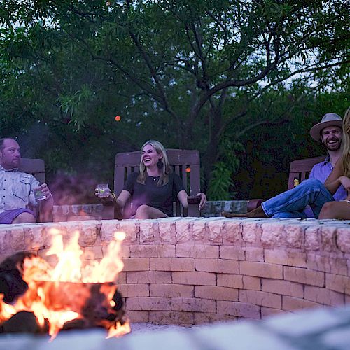 Four people are sitting around an outdoor fire pit in a relaxed, friendly setting.