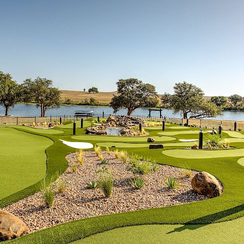 A lush mini-golf course is pictured, featuring landscaped greens, rocks, and plants, with a serene lake and tree-lined shore in the background.