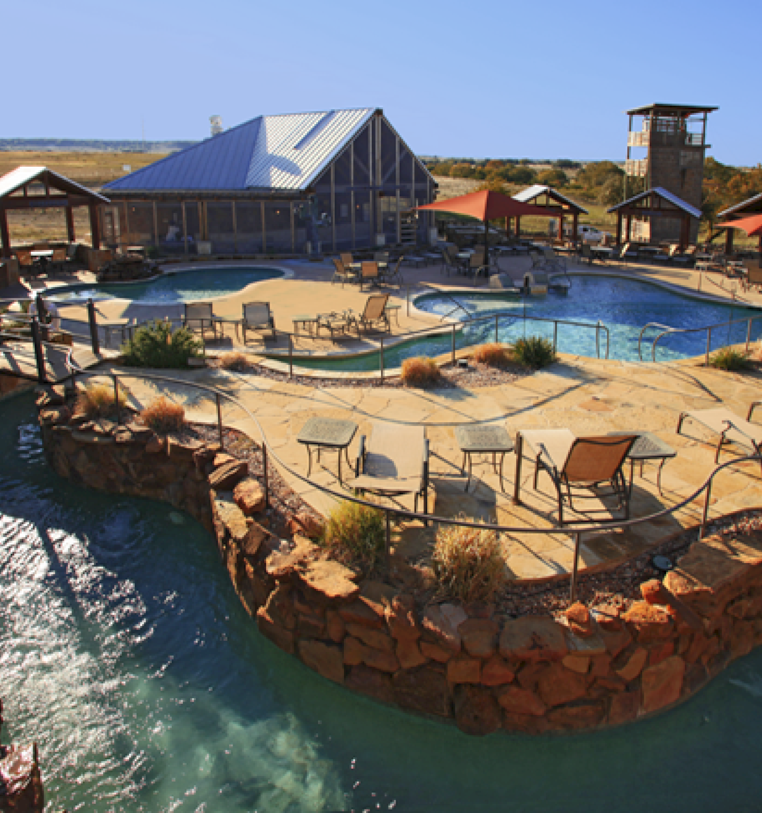 The image shows a resort with multiple pools, lounge chairs, a lazy river, and a large building in the background.