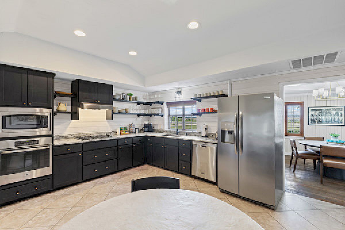 A modern kitchen with dark cabinets, stainless steel appliances, a marble counter, and adjacent dining area is pictured.