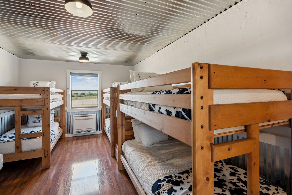 The image shows a bright room with four wooden bunk beds, a window, and a white and metallic ceiling.