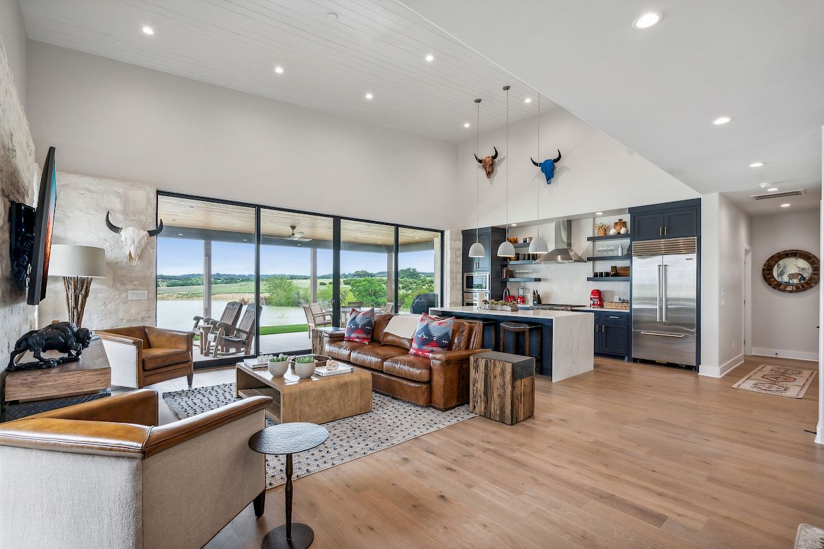 Spacious living room with modern kitchen, leather and fabric seating, decor, large windows with views, and wooden floors.