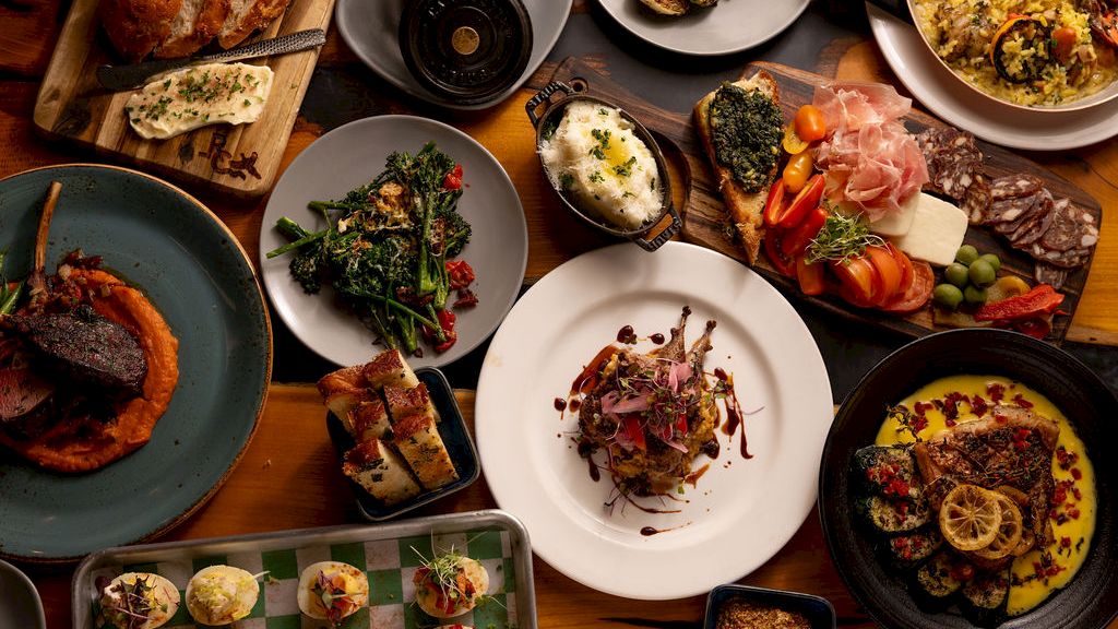 A spread of gourmet dishes&mdash;roasted potatoes, mussels, seafood, bread, veggies, and a steak&mdash;laid out on a dining table, ready to eat!