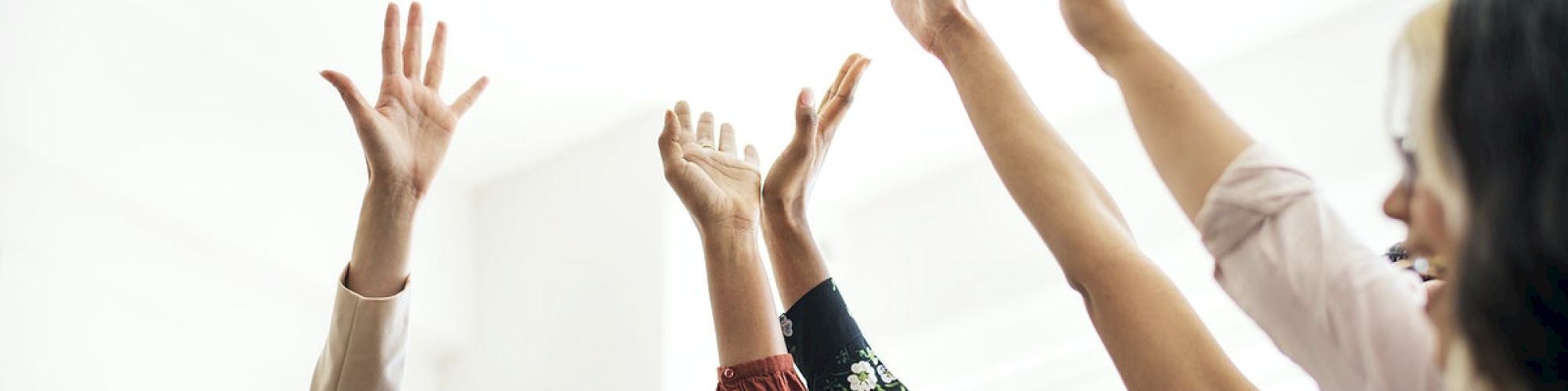 A group of people are raising their hands and smiling, appearing happy and cheerful in a well-lit room, possibly celebrating or participating in a team activity.