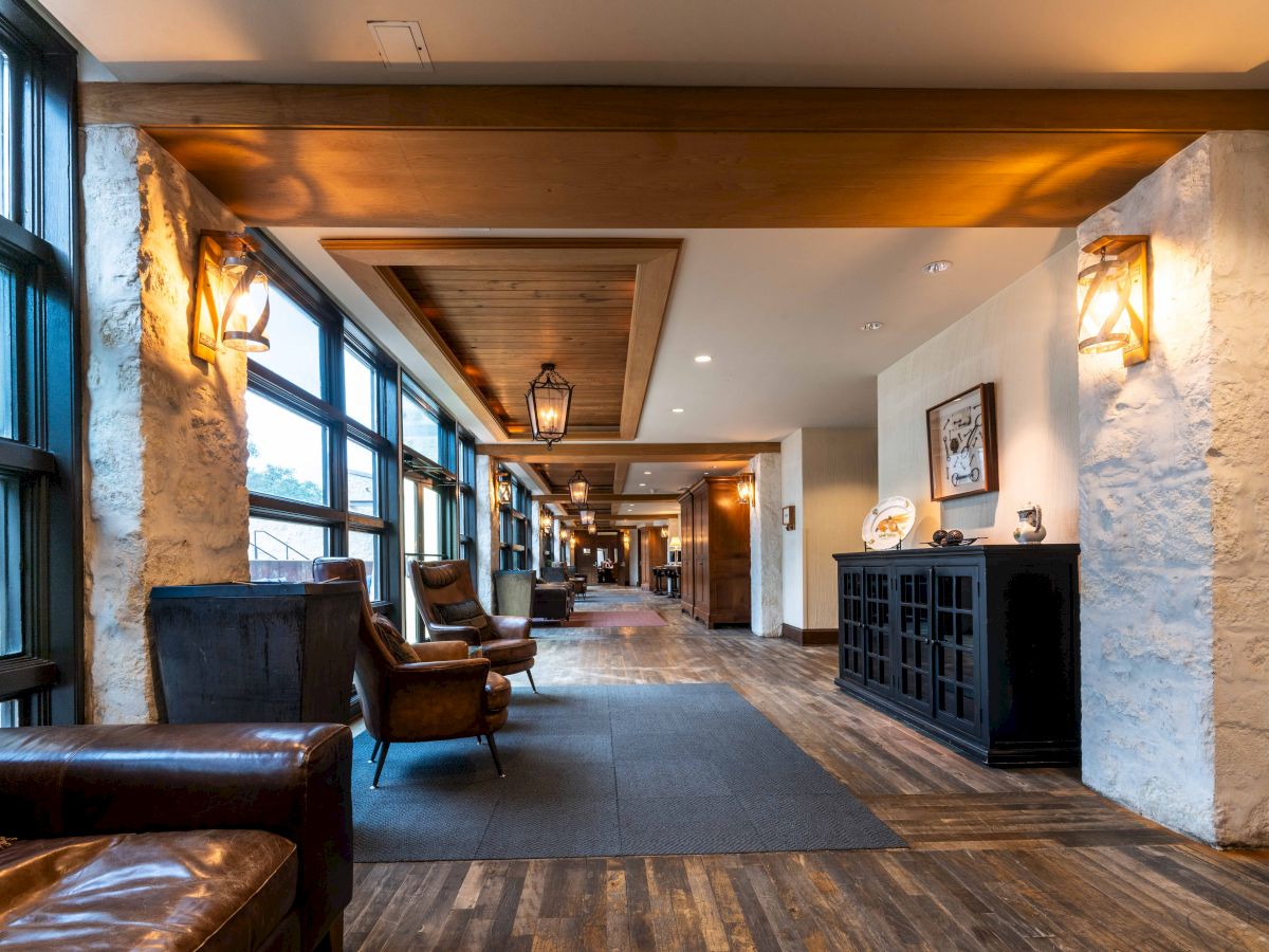 A cozy hallway with leather chairs, wooden floors, decorative lighting, and large windows, creating a warm and inviting atmosphere.
