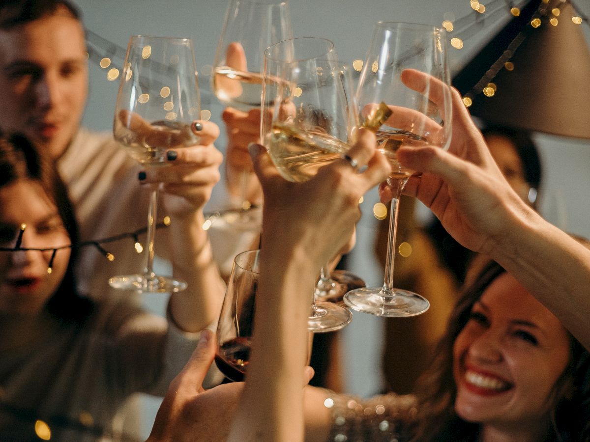 A group of people raising wine glasses in a toast, surrounded by festive lights, with smiles and laughter filling the scene.