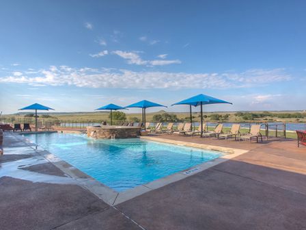 A serene outdoor pool area with blue umbrellas, sun loungers, and a scenic view of a lake and open landscape in the background.