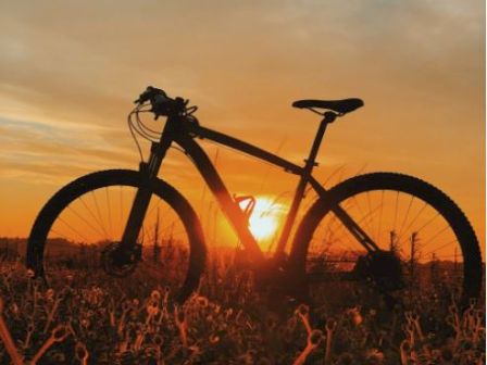 A bicycle is silhouetted against a stunning sunset in an open field, with the sky painted in warm hues of orange and yellow.