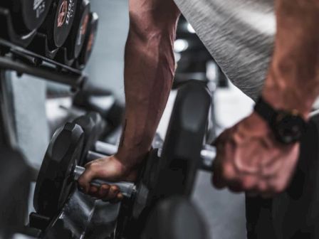 A person wearing a watch is lifting a dumbbell in a gym, with a rack of weights visible in the background.