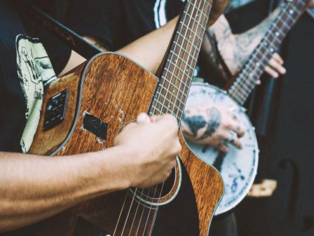 Two individuals are playing musical instruments, one with a guitar and the other with a banjo visible in the background.