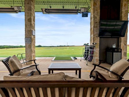 An open pavilion with patio chairs and a small table, overlooking green fields through a wide door.