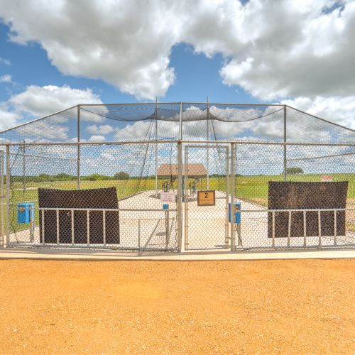 A fenced metal structure with netting, possibly an enclosure or batting cage, under a cloudy sky.
