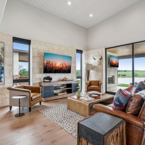 A modern living room with leather sofas, abstract art, and floor-to-ceiling windows overlooking a scenic outdoor view.