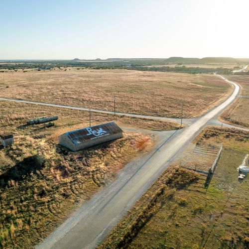 A winding road cuts through barren, rocky terrain with a lone car parked by the side, under a vast, cloudy sky.