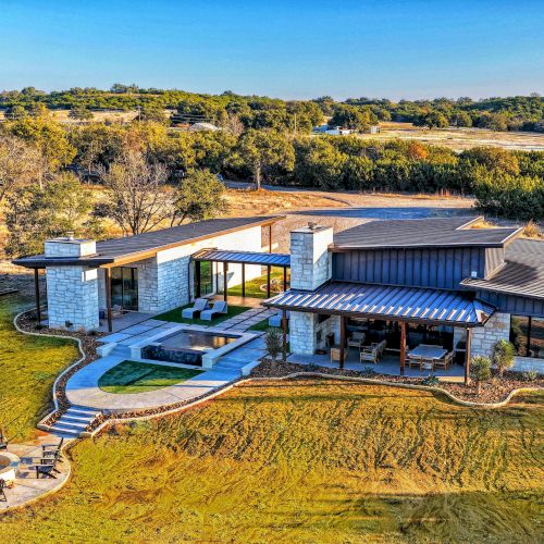 A modern single-story house with a flat roof, large windows, and a boat dock by a calm lake.