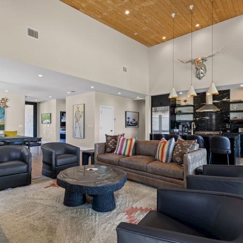 A spacious living area features a cozy seating arrangement, modern kitchen, and dining table, with a high ceiling and artistic decor.