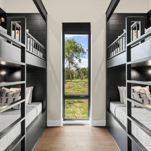 The image shows a room with black bunk beds on either side, a tall window in the center, and a view of trees outside.