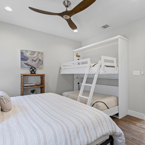 A bedroom with a double bed, bunk beds, ceiling fan, and wooden floor, featuring soft lighting and a minimalistic design.