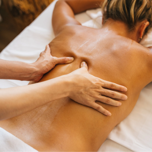 The image shows a person receiving a back massage from a masseuse, lying face down on a massage table.