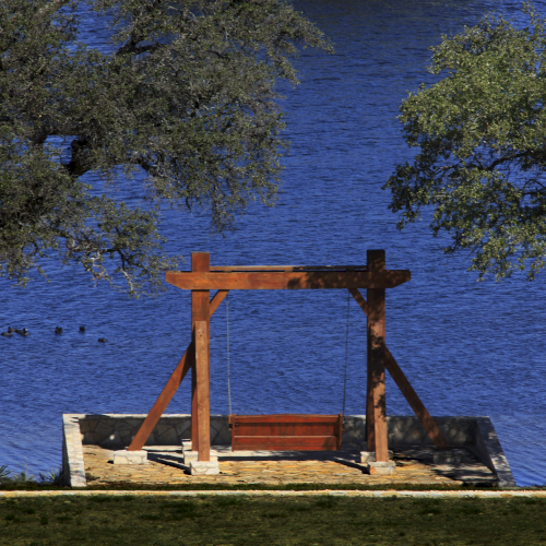 A wooden structure by a lake with surrounding trees and ducks on the water.