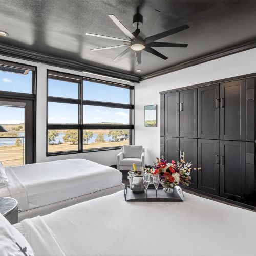 A modern, open-plan living space with a gray sofa, coffee table, and large windows. Staircase and industrial-style beams add character.