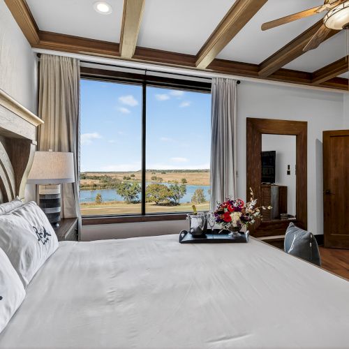 Luxurious hotel suite with a king bed, exposed wooden beams, large windows, and a scenic mountain view. Top it at 140 characters, always ending the sentence.