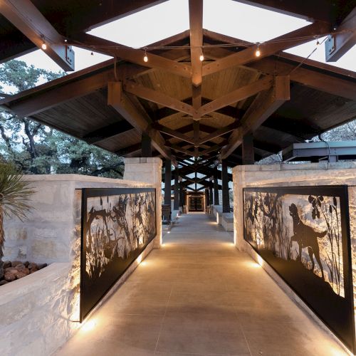 A covered walkway with warm lighting, stone walls, and panels featuring wildlife images, leading to a distant arched corridor.