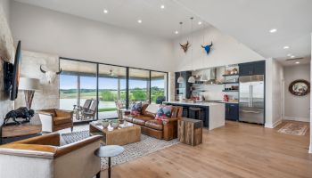 A modern living room with leather seating, open-plan kitchen, bull skull decor, and large windows overlooking a scenic view.