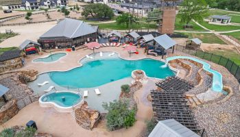 An aerial view of a resort with large turquoise swimming pools, hot tub, playground, and landscaped grounds.
