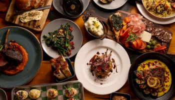 A spread of gourmet food: breads, roasted vegetables, mushrooms, steak, seafood, and charcuterie on a rustic table of plates and bowls.