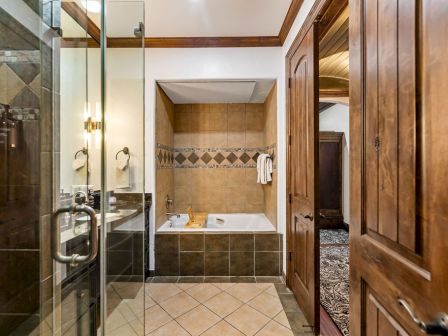 A luxurious bathroom with glass shower, tiled walls, a white bathtub, wooden doors, and a warm, polished interior.