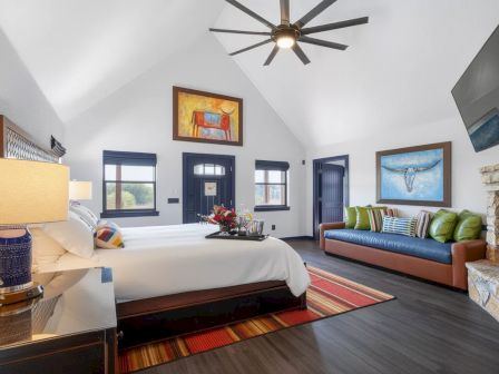 A bright modern room with a bed, bedside lamp, colorful rug, green-and-blue sofa, and a stone fireplace.