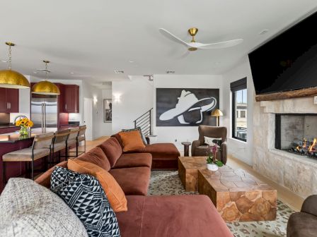A modern living room with a brown sectional, stone fireplace, kitchen area, ceiling fan, and framed astronaut wall art.