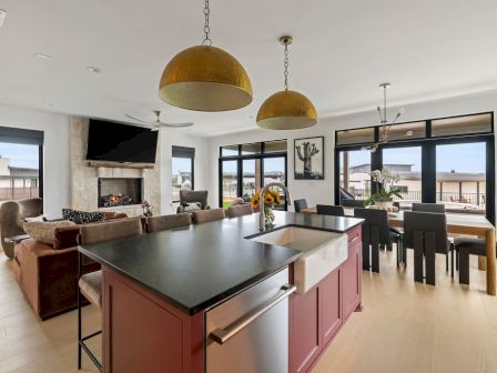 Bright modern living/dining area with a kitchen island, couches, TV/fireplace, and golden pendant lights.