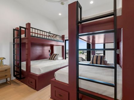 A modern bedroom with two stacked bunk beds and pillows, lit by recessed ceiling lights.