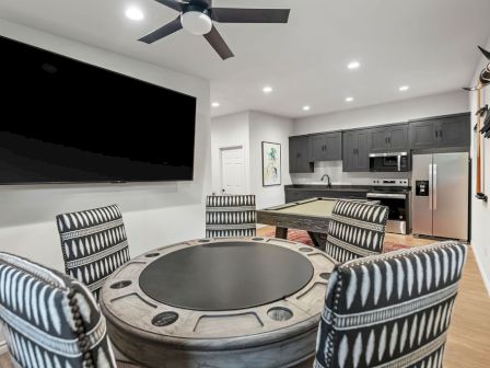 A modern kitchen/dining space with striped chairs, a wall TV, and a robot vacuum on the floor.