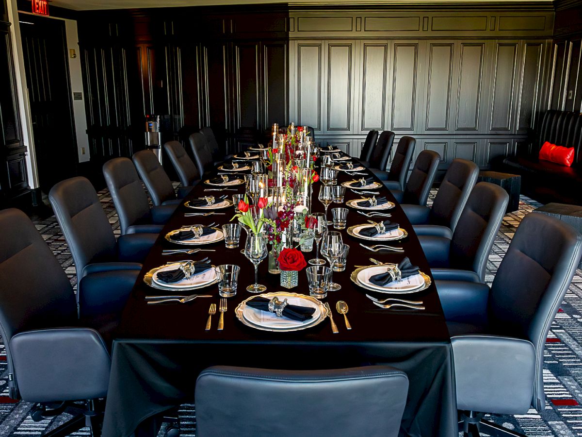 A formal meeting room set with a long banquet table, neatly placed place settings, glassware, and a flower centerpiece.