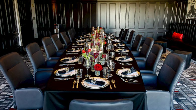 A formal meeting room set with a long banquet table, neatly placed place settings, glassware, and a flower centerpiece.