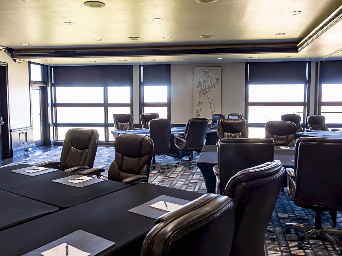 A modern office conference room with leather chairs, conference tables, large windows, and a wall mural in the background.