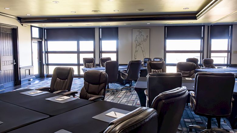 A modern office conference room with leather chairs, conference tables, large windows, and a wall mural in the background.