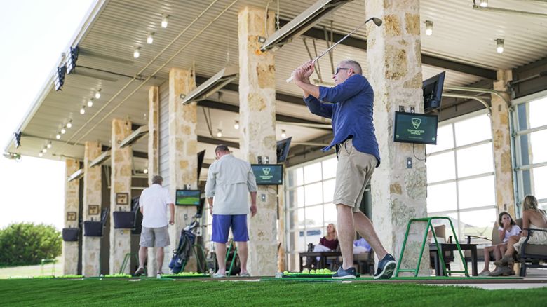 People are engaged in golfing activities at a driving range. Others are observing or preparing for their turn while enjoying the facility.