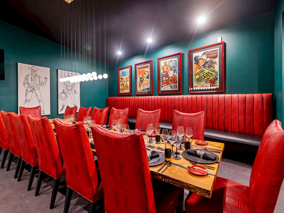 A cozy restaurant booth with red velvet seating, a set dining table, and framed movie-style posters on the wall.