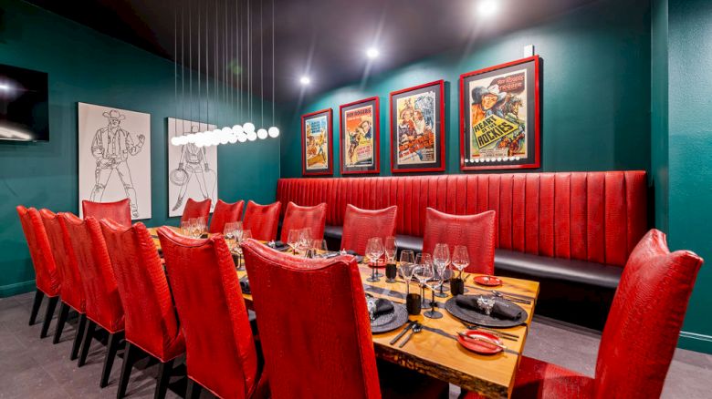 A cozy restaurant booth with red velvet seating, a set dining table, and framed movie-style posters on the wall.