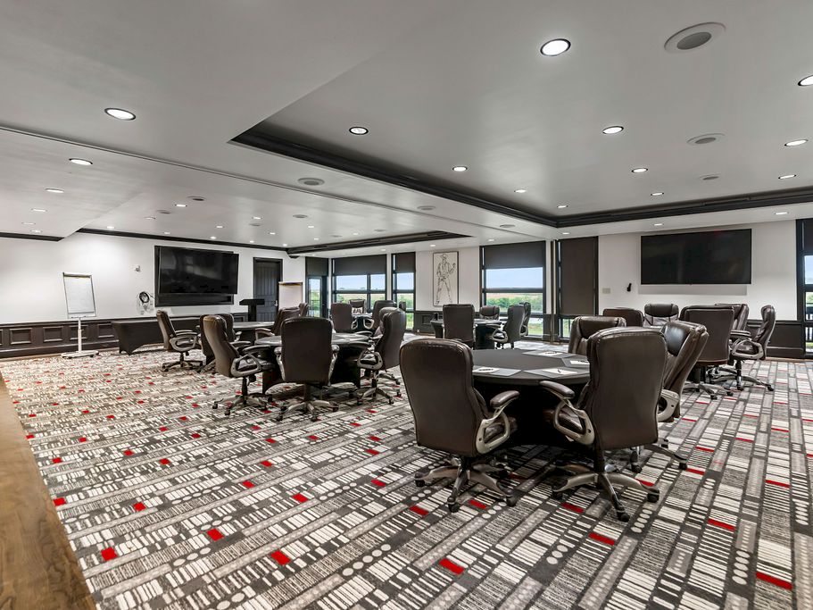 A modern conference room with rows of swivel chairs, patterned carpet, and large windows overlooking greenery.