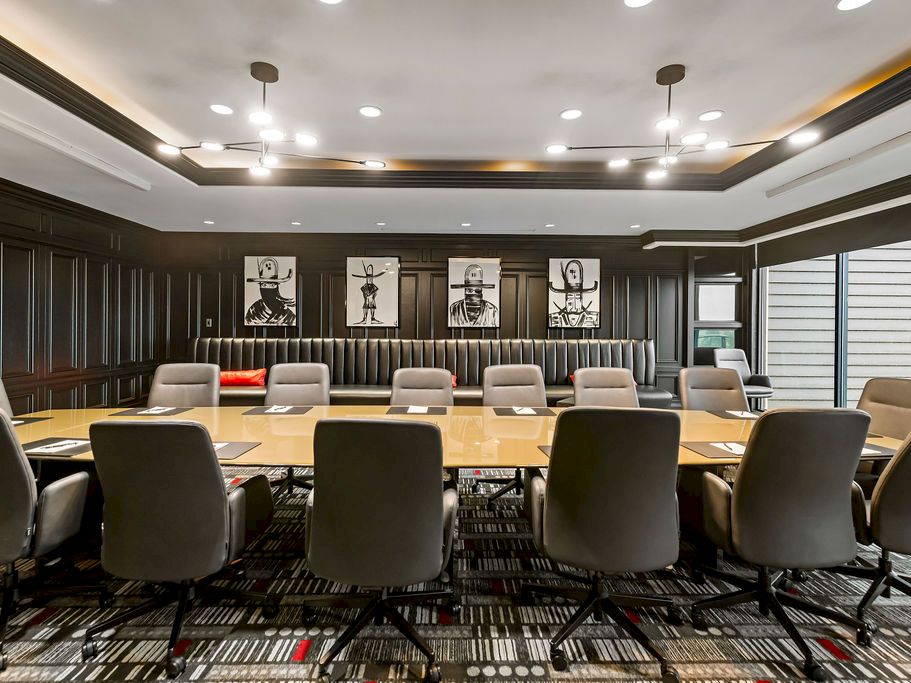 A modern conference room with long wooden meeting tables and rows of chairs, lit by recessed ceiling lights.