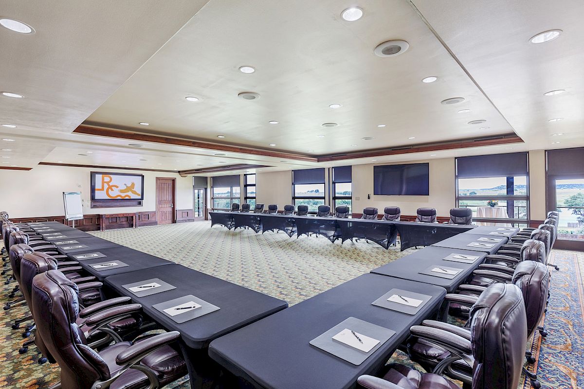 A spacious conference room with U-shaped table setup, leather chairs, projection screen, and bright lighting.